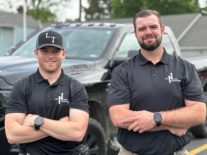 Lift N Take owners standing proudly in front of their hauling truck
